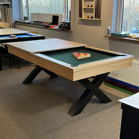 Pool table with a green felt surface and wooden frame in a room with windows and shelves.